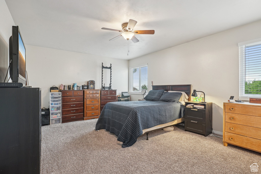 Bedroom with light colored carpet, a ceiling fan, and a desk
