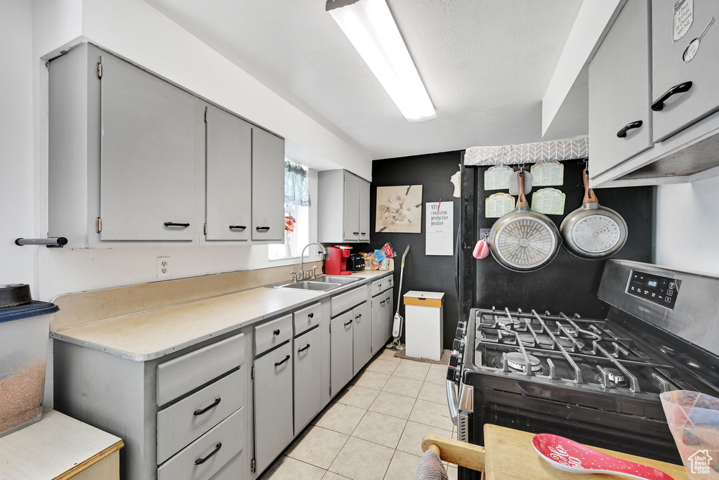 Kitchen with gas stove, a sink, gray cabinets, light countertops, and light tile patterned floors