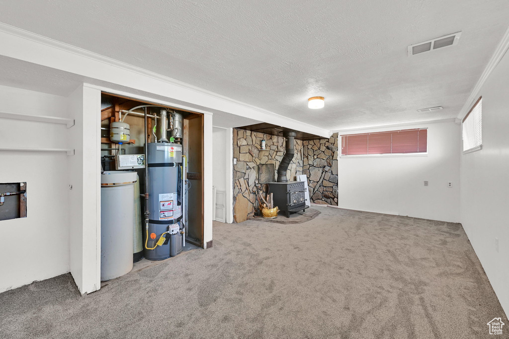 Basement featuring strapped water heater, a wood stove, carpet, a textured ceiling, and a water softener