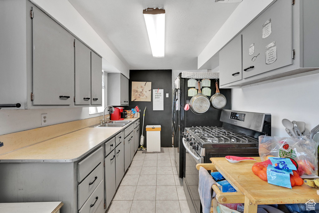 Kitchen featuring a sink, gas range, gray cabinets, light countertops, and light tile patterned floors