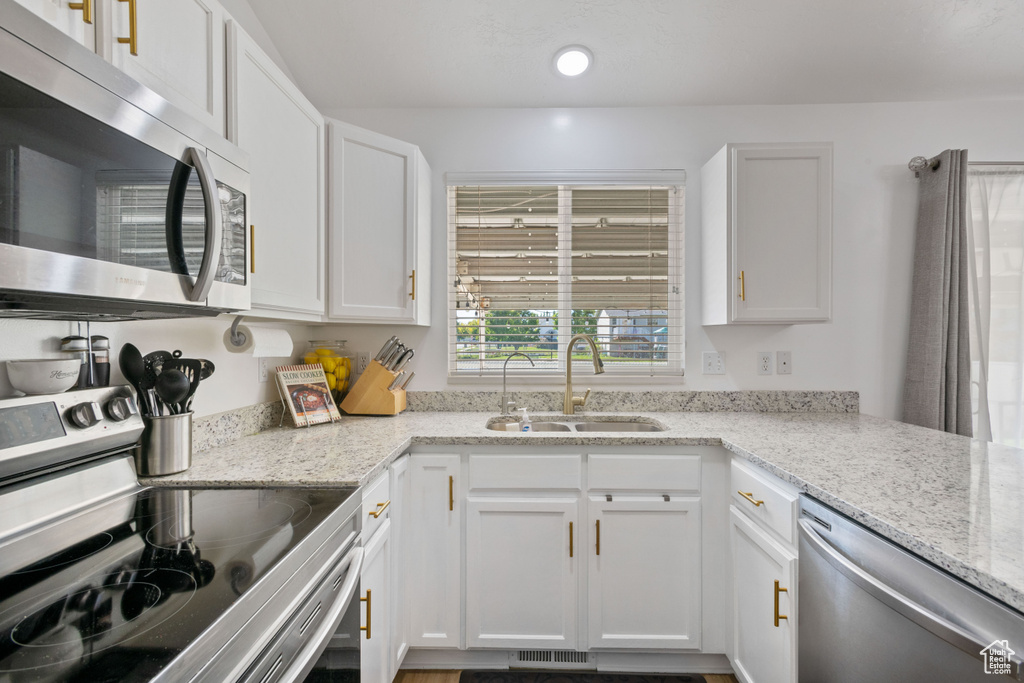 Kitchen with stainless steel appliances, a sink, white cabinets, light stone countertops, and recessed lighting