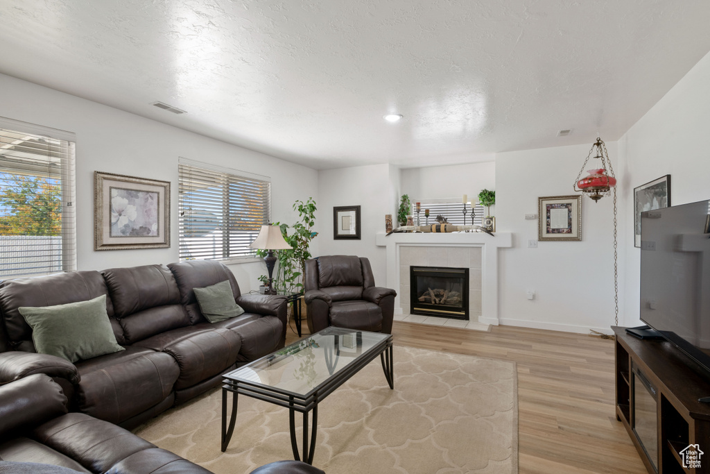 Living room with light wood-type flooring, a tiled fireplace, and baseboards