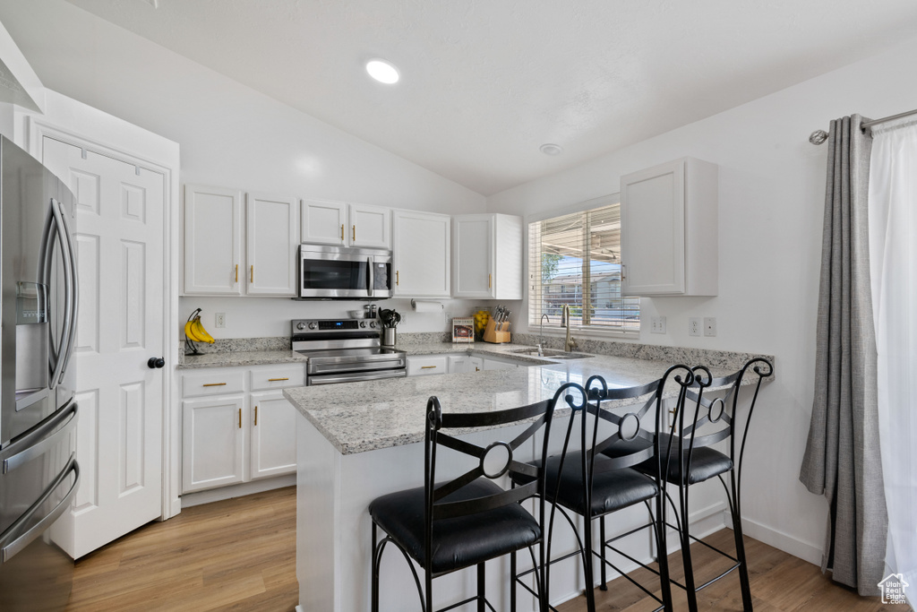 Kitchen featuring stainless steel appliances, a sink, a kitchen breakfast bar, vaulted ceiling, and white cabinets