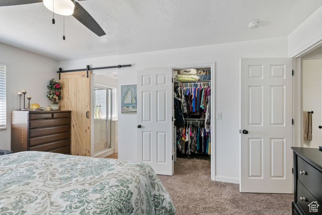 Bedroom featuring a barn door, light carpet, a spacious closet, a closet, and a ceiling fan