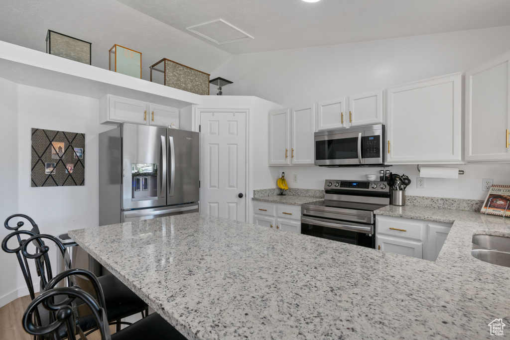 Kitchen featuring stainless steel appliances, white cabinets, vaulted ceiling, and light stone counters