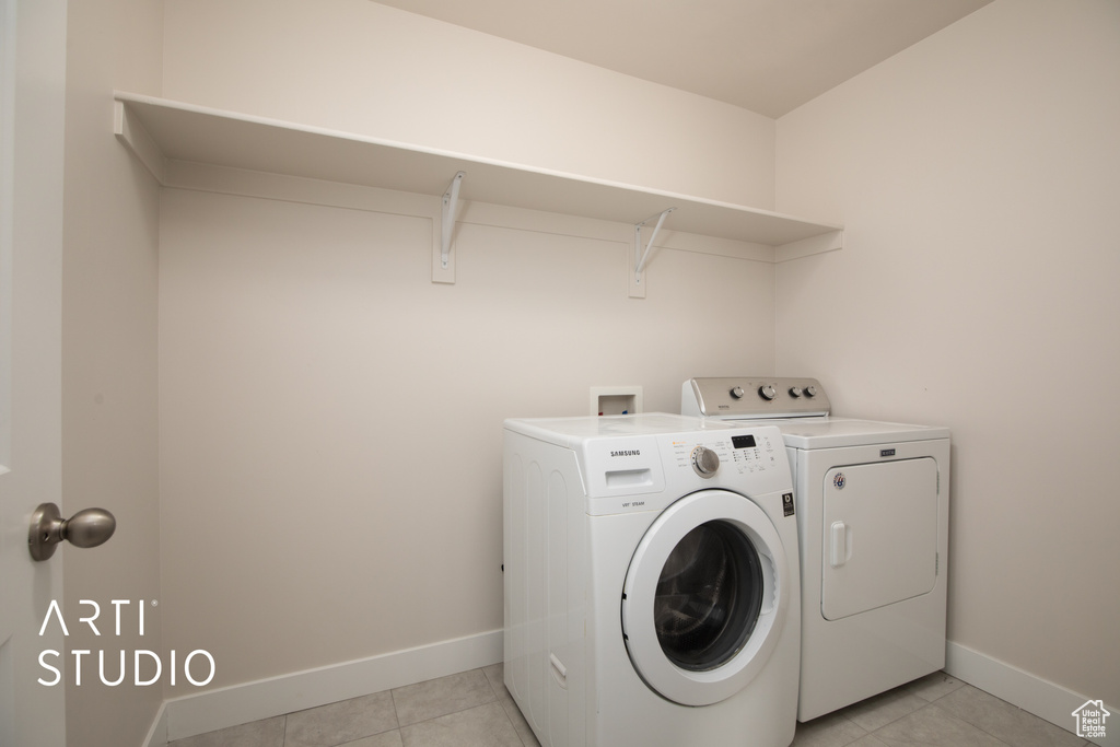 Laundry area with separate washer and dryer, light tile patterned floors, and baseboards