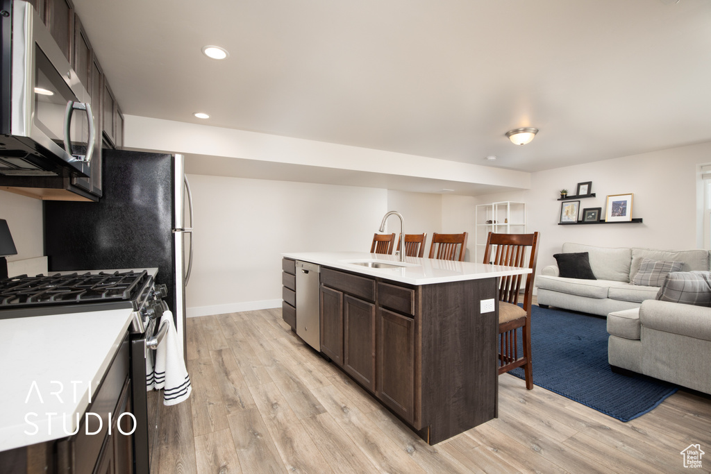Kitchen featuring appliances with stainless steel finishes, a sink, dark brown cabinetry, light wood-type flooring, and recessed lighting