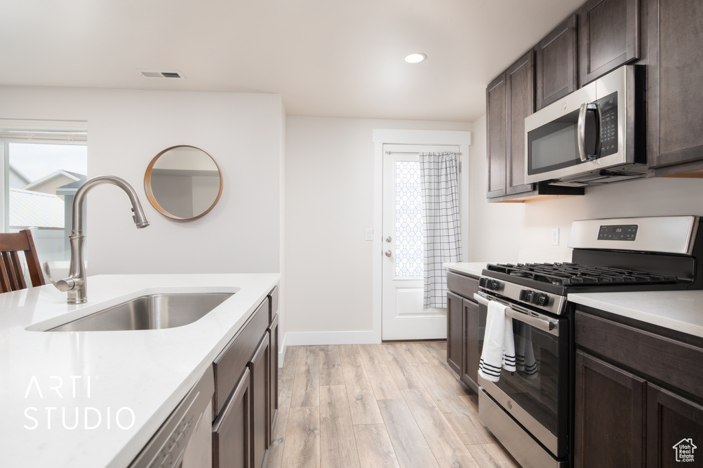 Kitchen featuring appliances with stainless steel finishes, a sink, dark brown cabinets, light wood finished floors, and light countertops