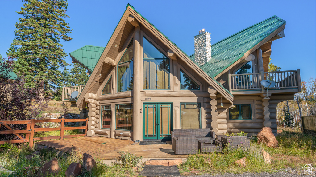 Back of property with a chimney, metal roof, a deck, a balcony, and log exterior
