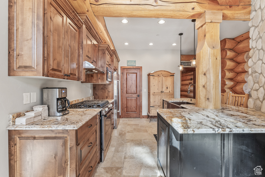 Kitchen with stone finish flooring, a sink, log walls, under cabinet range hood, and appliances with stainless steel finishes