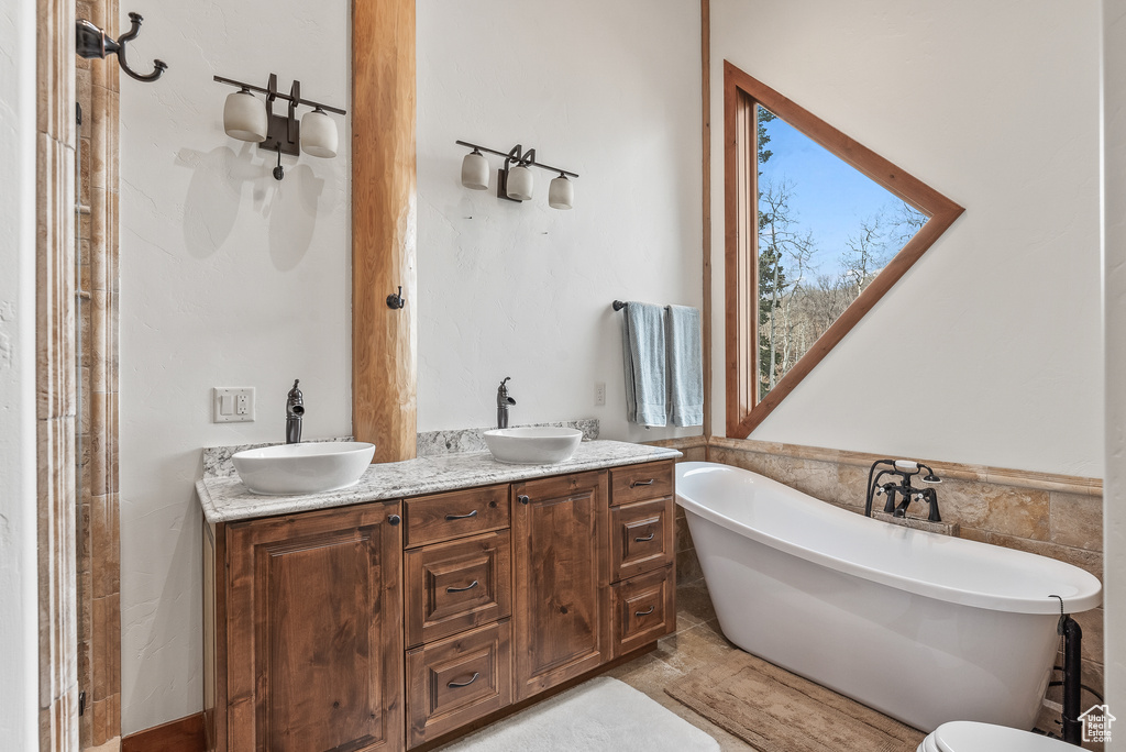 Full bath featuring double vanity, a freestanding bath, tile walls, and a sink
