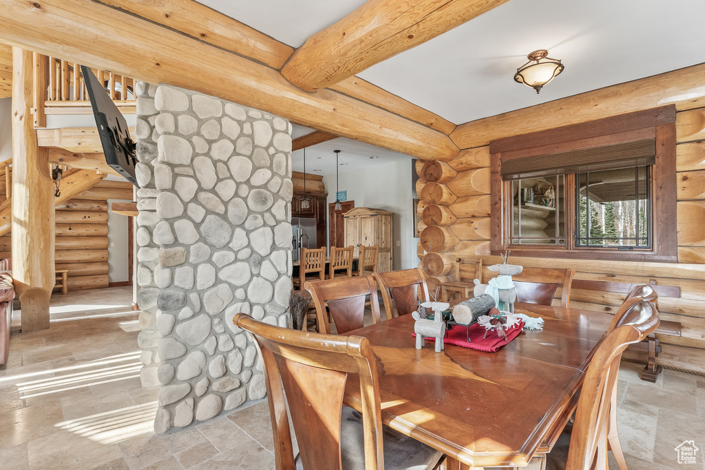 Dining room featuring beam ceiling, log walls, stone finish flooring, and stairs
