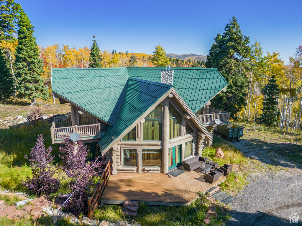 Back of house with log siding, a balcony, metal roof, a chimney, and a standing seam roof
