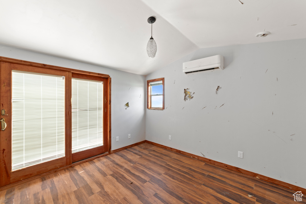 Empty room with an AC wall unit, wood finished floors, vaulted ceiling, and baseboards