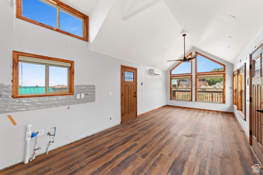 Unfurnished living room with wood finished floors, a ceiling fan, vaulted ceiling, and a wall mounted AC