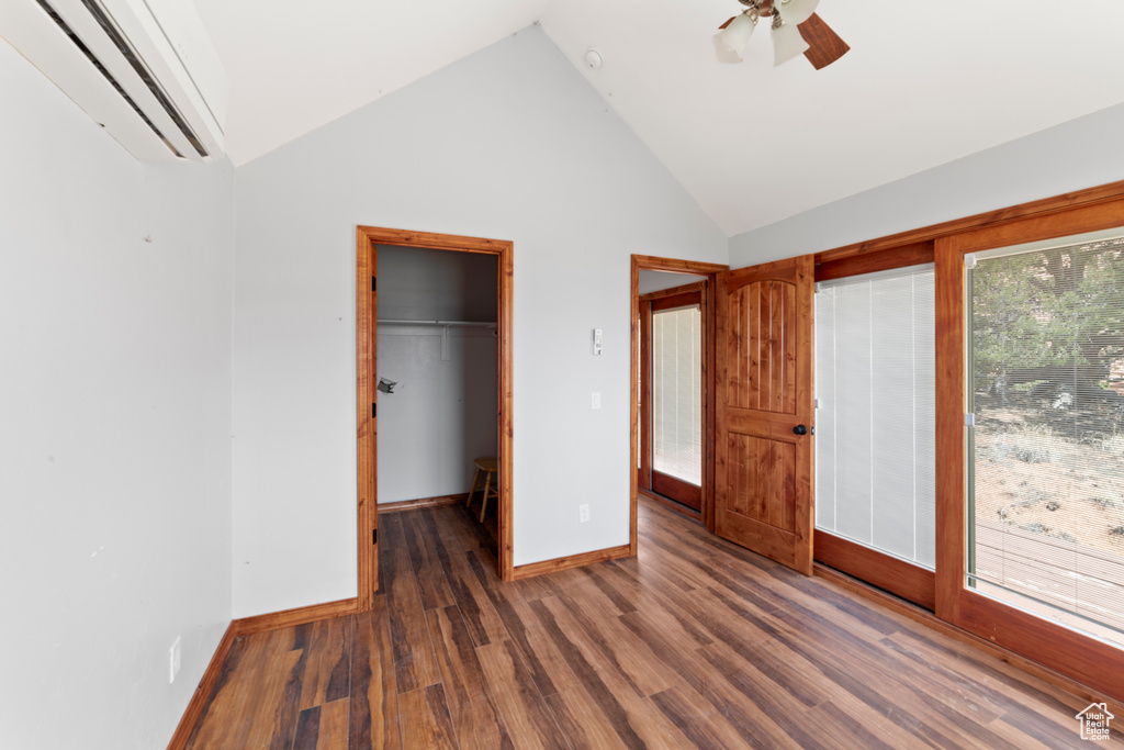 Unfurnished bedroom featuring an AC wall unit, wood finished floors, baseboards, a walk in closet, and ceiling fan