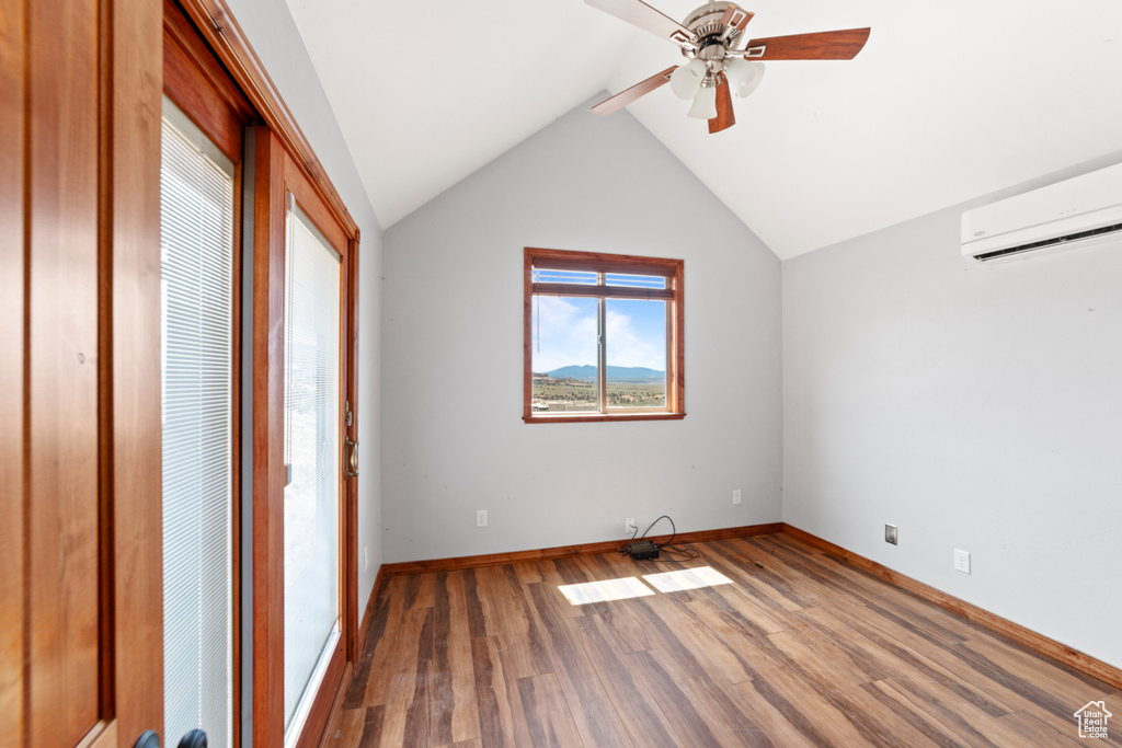 Unfurnished bedroom featuring a wall unit AC, wood finished floors, vaulted ceiling, baseboards, and a ceiling fan