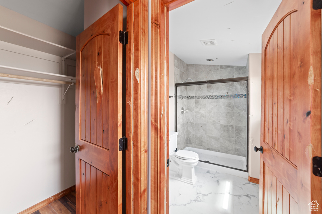 Full bath with a shower stall, marble look tiles, toilet, and baseboards