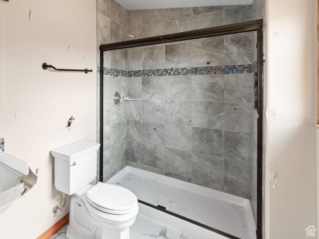 Bathroom featuring a stall shower, toilet, marble look tiles, and a sink