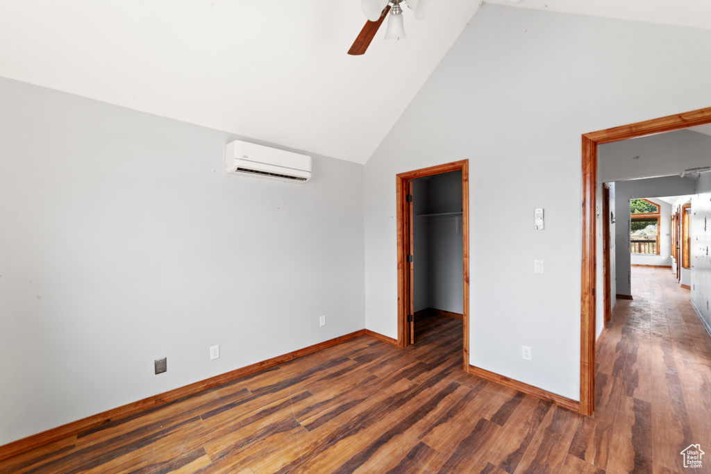 Unfurnished bedroom with a wall mounted air conditioner, wood finished floors, high vaulted ceiling, baseboards, and a walk in closet