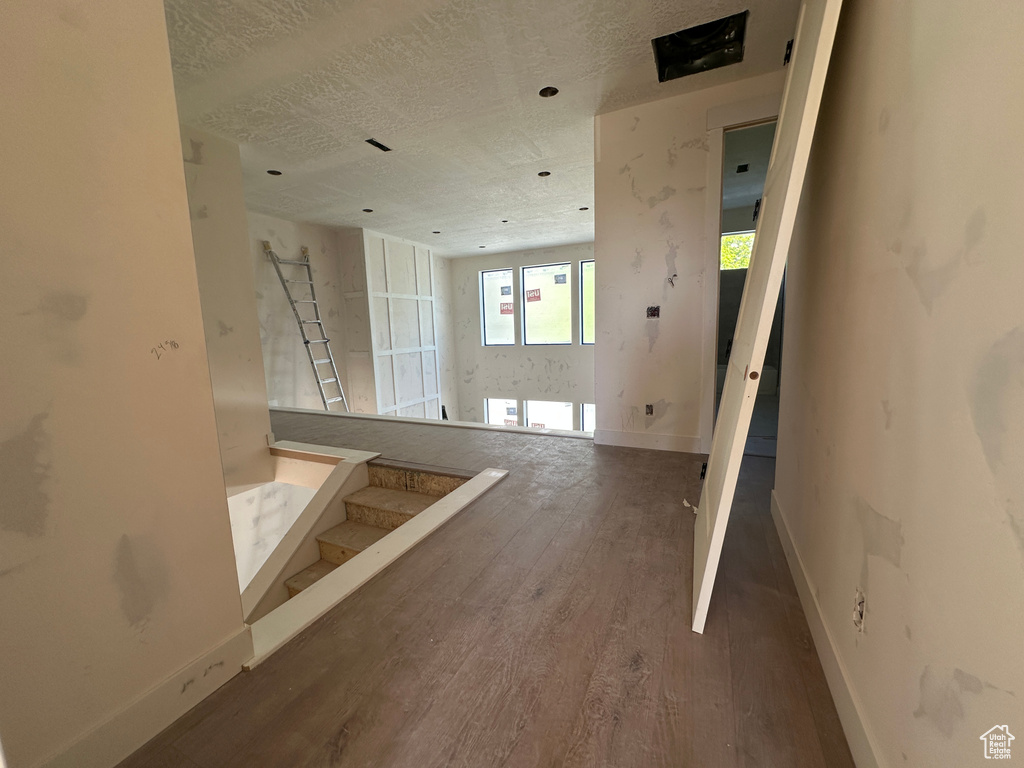 Unfurnished living room with wood finished floors, baseboards, a textured ceiling, and stairway