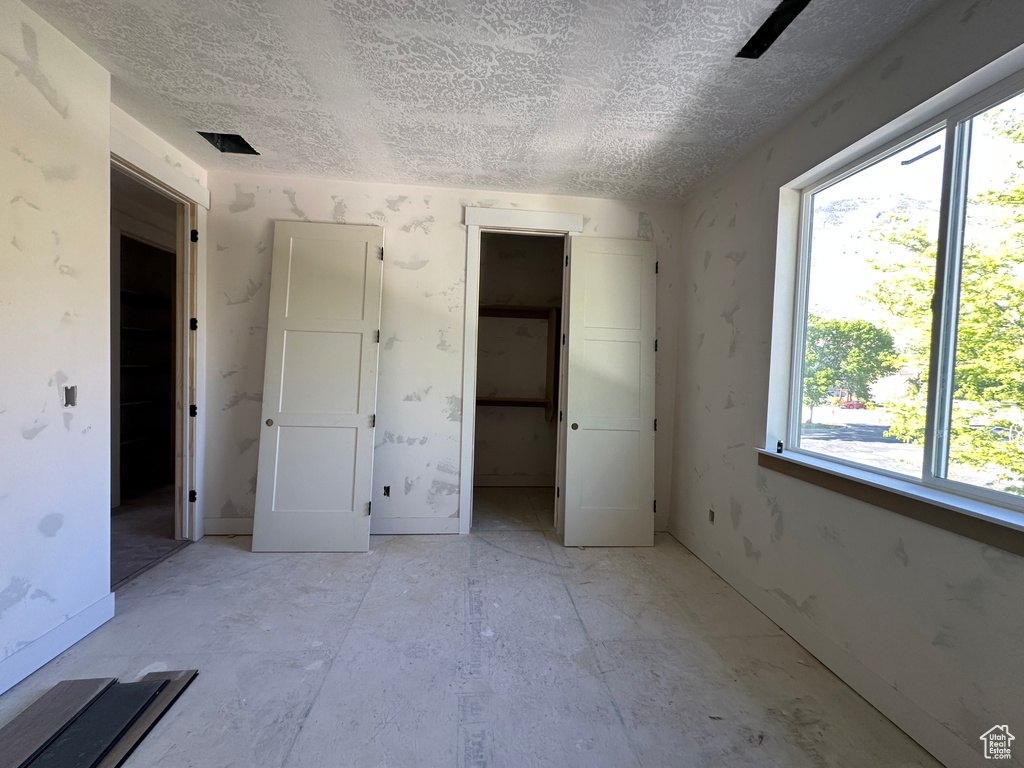 Unfurnished bedroom with a textured ceiling, multiple windows, a walk in closet, and a closet
