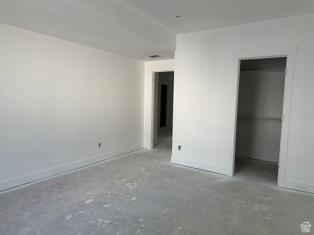 Unfurnished bedroom with concrete floors, baseboards, a walk in closet, and a closet