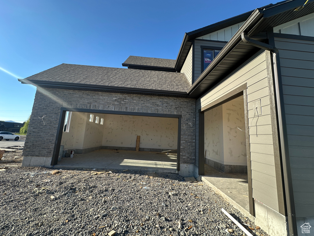 View of side of property featuring brick siding, a garage, roof with shingles, driveway, and board and batten siding