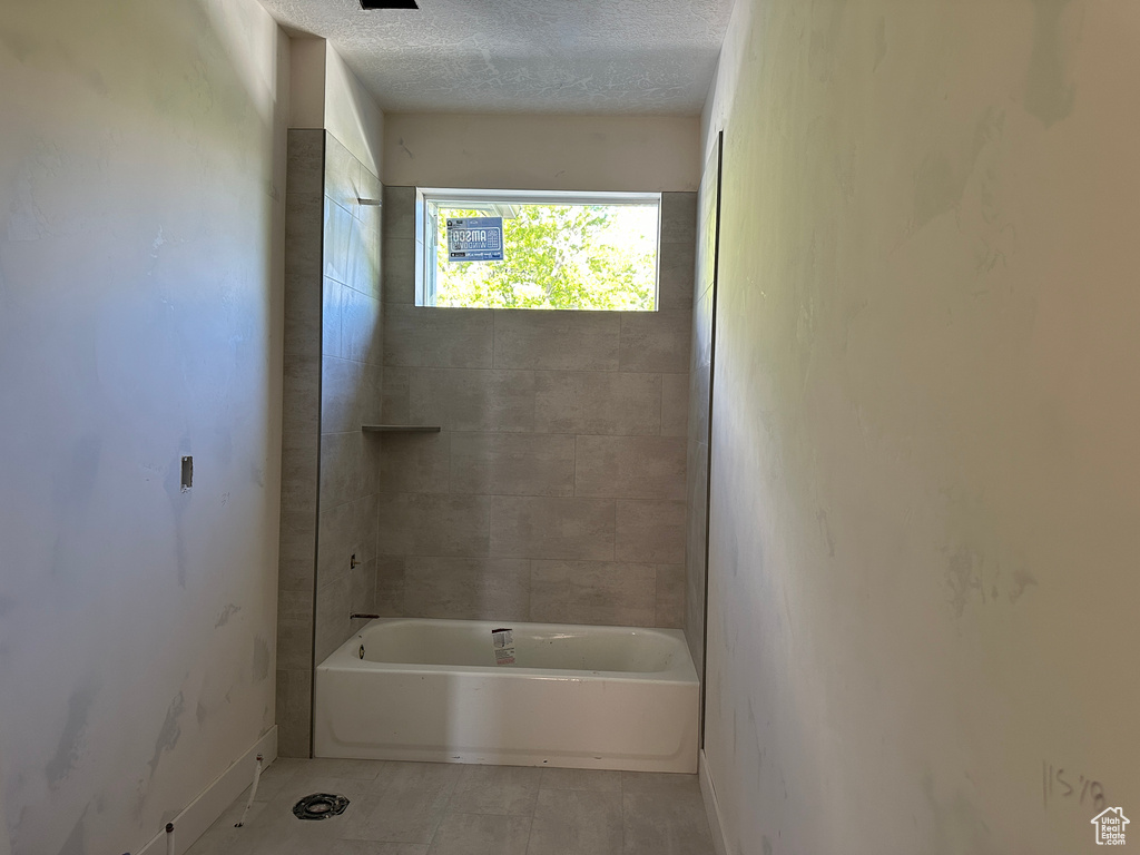 Bathroom with baseboards, tile patterned floors, a textured ceiling, and washtub / shower combination