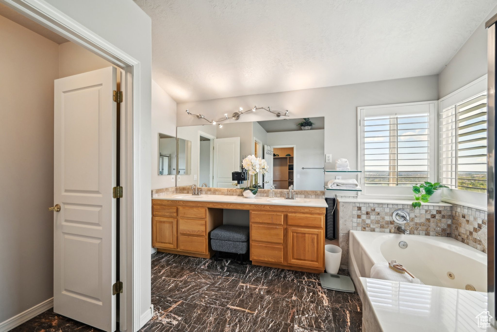 Full bath with a jetted tub, double vanity, and marble look tile flooring