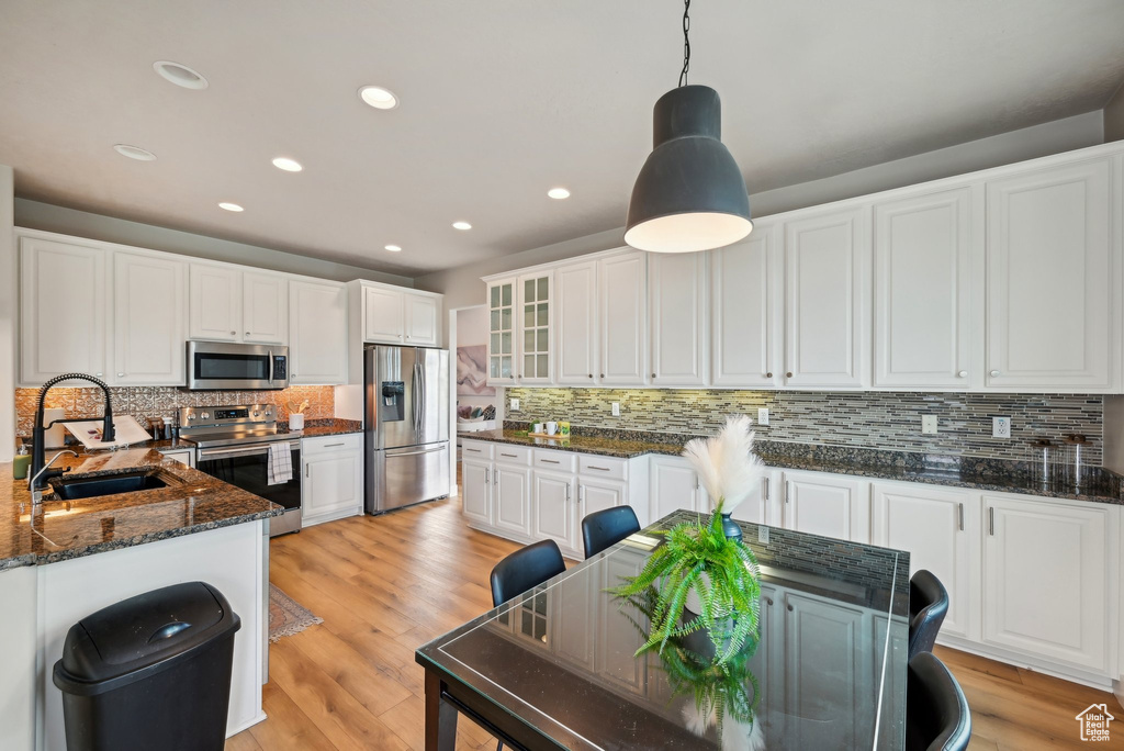 Kitchen with appliances with stainless steel finishes, a sink, tasteful backsplash, white cabinetry, and glass insert cabinets