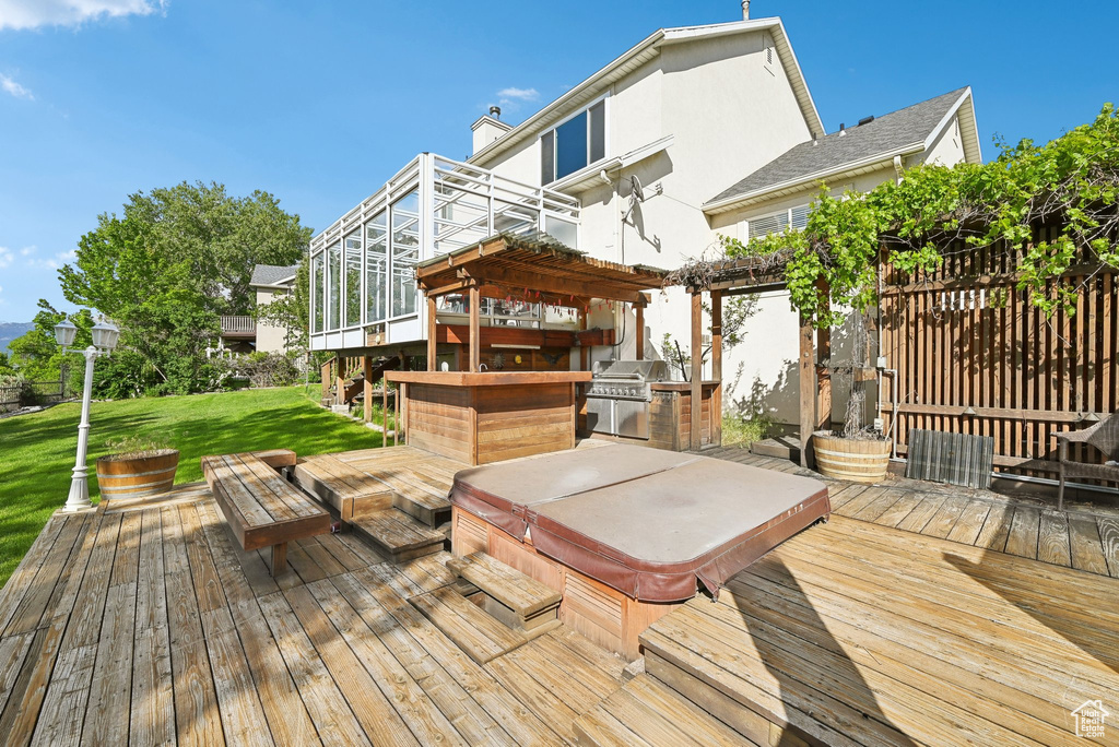 Wooden deck featuring a covered hot tub, a lawn, and an outdoor kitchen