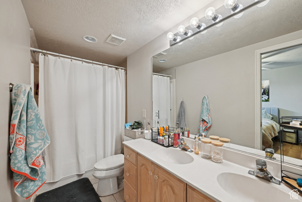 Ensuite bathroom featuring toilet, double vanity, a textured ceiling, tile patterned floors, and a shower with curtain