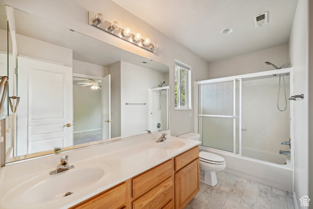 Bathroom featuring double vanity, toilet, bath / shower combo with glass door, and ceiling fan