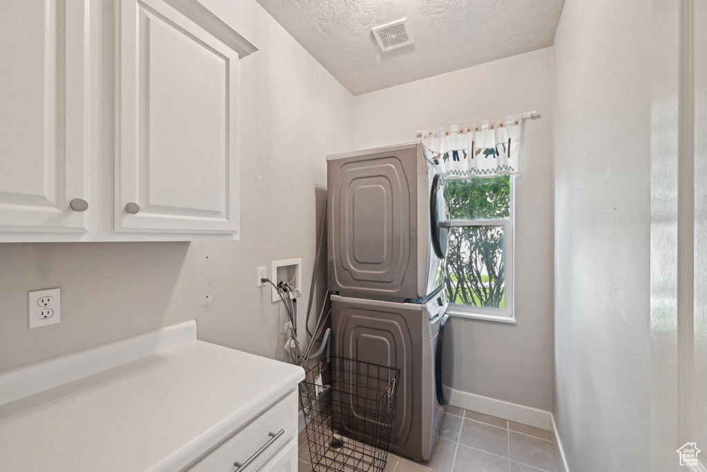 Laundry area with stacked washer / dryer, cabinet space, a textured ceiling, baseboards, and light tile patterned floors