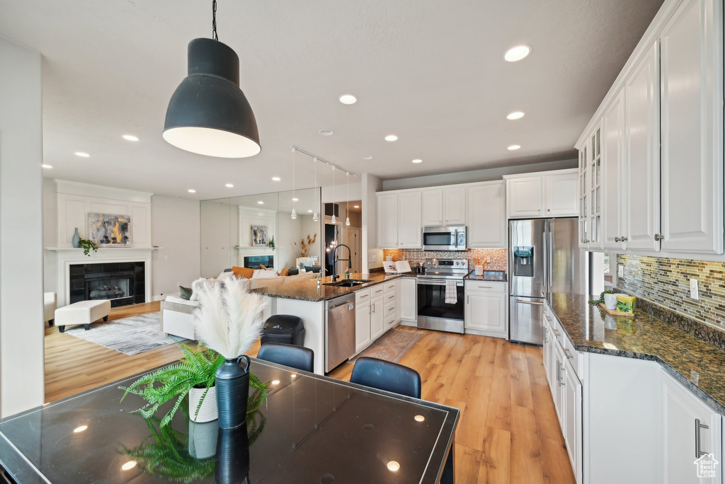 Kitchen featuring stainless steel appliances, a sink, light wood-style flooring, white cabinetry, and decorative backsplash