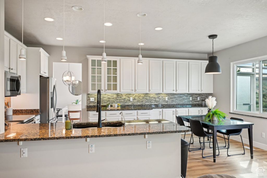 Kitchen featuring stainless steel appliances, a sink, dark stone counters, light wood finished floors, and white cabinets