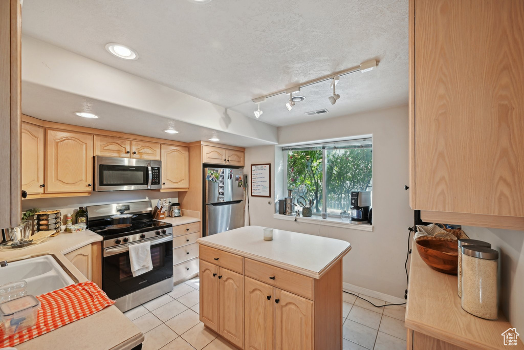 Kitchen with appliances with stainless steel finishes, light brown cabinets, light countertops, light tile patterned flooring, and a kitchen island