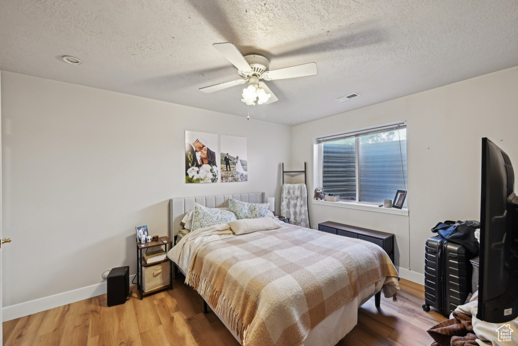Bedroom with wood finished floors, baseboards, a textured ceiling, and a ceiling fan