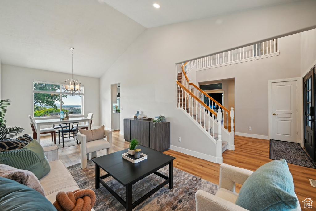 Living area with stairway, high vaulted ceiling, baseboards, a chandelier, and wood finished floors