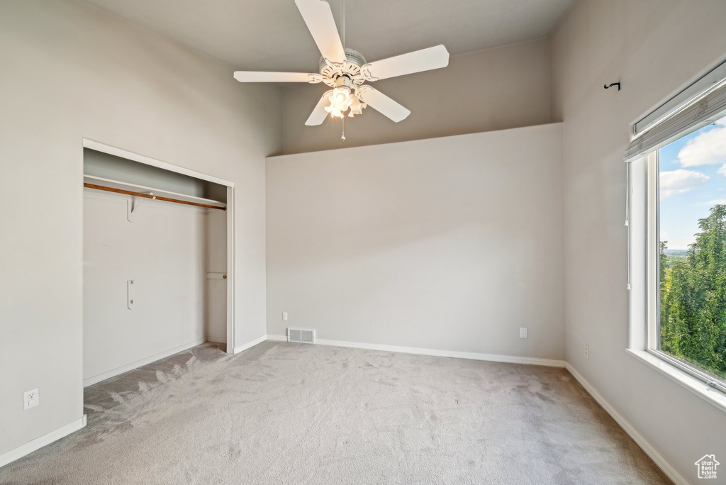 Unfurnished bedroom featuring multiple windows, carpet floors, a closet, and a high ceiling