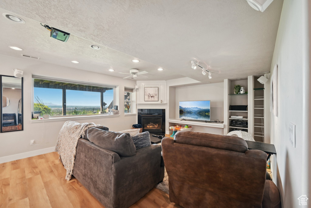 Living room with light wood-type flooring, recessed lighting, a glass covered fireplace, baseboards, and ceiling fan