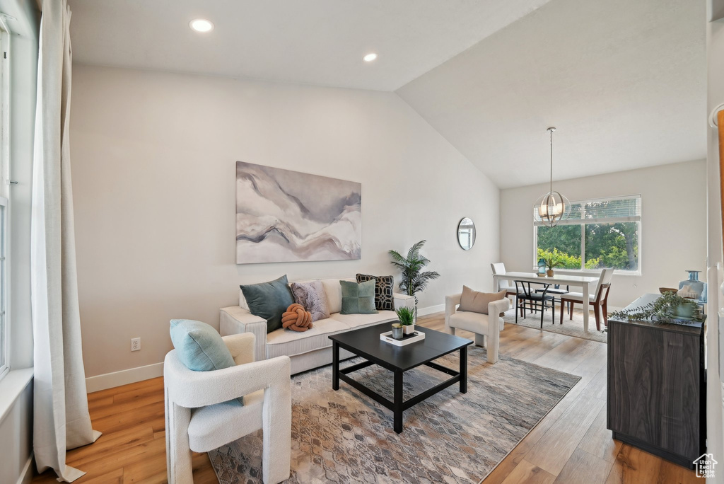 Living room with vaulted ceiling, light wood finished floors, baseboards, recessed lighting, and a chandelier