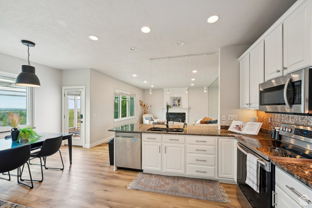 Kitchen with stainless steel appliances, a peninsula, white cabinets, recessed lighting, and light wood-type flooring