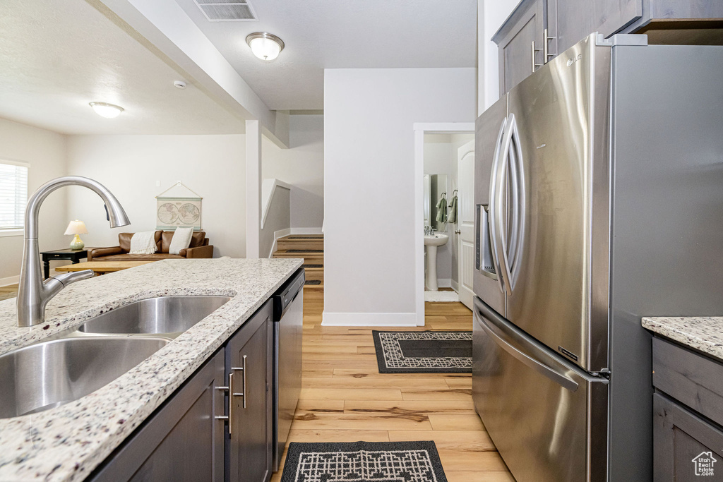 Kitchen featuring stainless steel appliances, a sink, light wood-style floors, baseboards, and light stone countertops