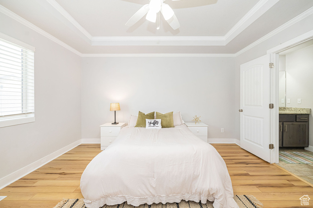 Bedroom with light wood-style flooring, a raised ceiling, connected bathroom, and crown molding