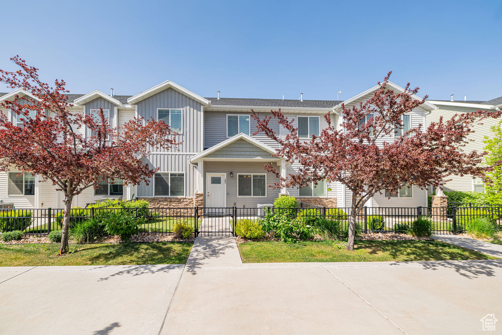 Townhome / multi-family property with board and batten siding, a fenced front yard, and stone siding