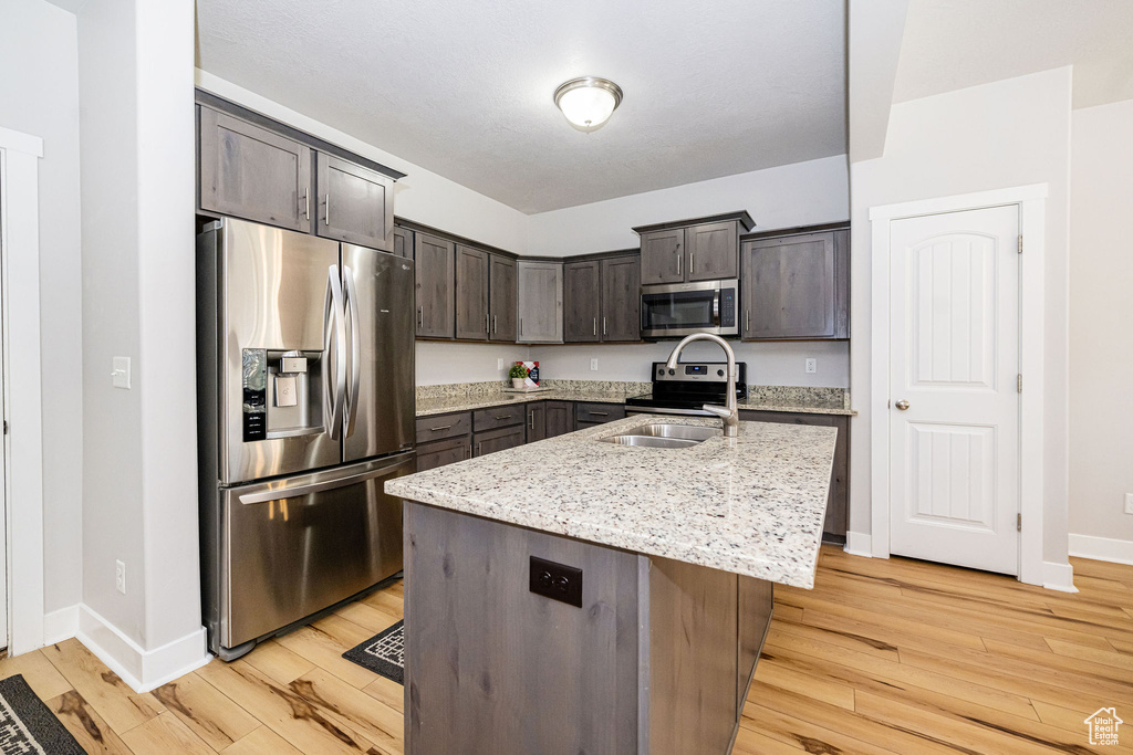 Kitchen with appliances with stainless steel finishes, light wood-style floors, dark brown cabinetry, and baseboards