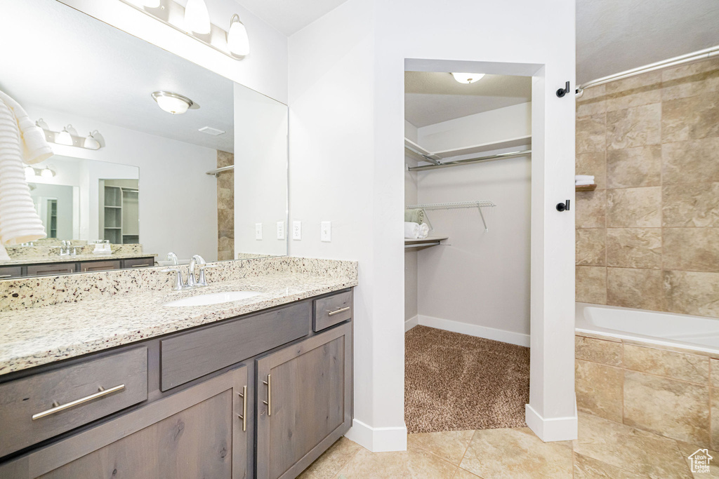 Bathroom featuring tile patterned floors, a spacious closet, vanity, baseboards, and tiled shower / bath combo