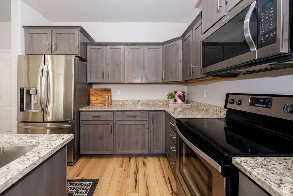 Kitchen featuring stainless steel appliances, light wood-type flooring, dark brown cabinetry, and light stone countertops